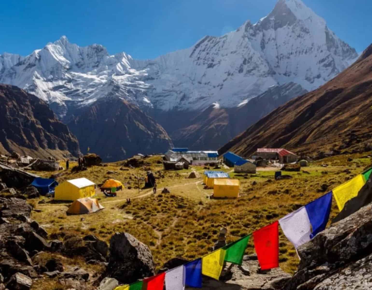 Mountain base camp with tents and prayer flags below snowy peaks